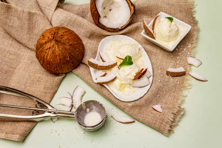 Lactose free coconut ice cream. Special spoon, halves of fruit, flakes. Vegan dessert concept. Light green backgroundの写真素材