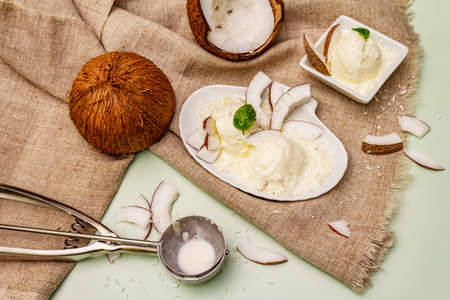 Lactose free coconut ice cream. Special spoon, halves of fruit, flakes. Vegan dessert concept. Light green backgroundの写真素材