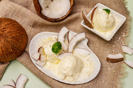 Lactose free coconut ice cream. Special spoon, halves of fruit, flakes. Vegan dessert concept. Light green backgroundの写真素材