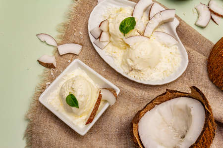Lactose free coconut ice cream. Special spoon, halves of fruit, flakes. Vegan dessert concept. Light green backgroundの写真素材