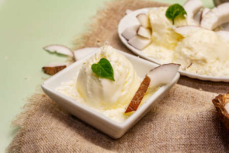 Lactose free coconut ice cream. Special spoon, halves of fruit, flakes. Vegan dessert concept. Light green backgroundの写真素材