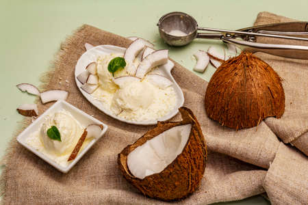 Lactose free coconut ice cream. Special spoon, halves of fruit, flakes. Vegan dessert concept. Light green backgroundの写真素材