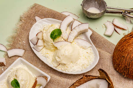 Lactose free coconut ice cream. Special spoon, halves of fruit, flakes. Vegan dessert concept. Light green backgroundの写真素材