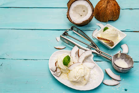 Lactose free coconut ice cream. Special spoon, halves of fruit, flakes. Vegan dessert concept. Trendy turquoise wooden boards background, top viewの写真素材