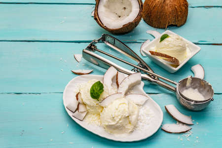 Lactose free coconut ice cream. Special spoon, halves of fruit, flakes. Vegan dessert concept. Trendy turquoise wooden boards backgroundの写真素材