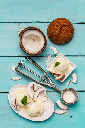 Lactose free coconut ice cream. Special spoon, halves of fruit, flakes. Vegan dessert concept. Trendy turquoise wooden boards backgroundの写真素材