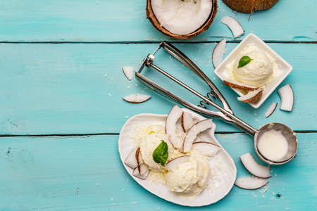 Lactose free coconut ice cream. Special spoon, halves of fruit, flakes. Vegan dessert concept. Trendy turquoise wooden boards background, top viewの写真素材