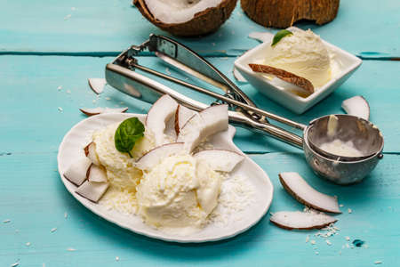 Lactose free coconut ice cream. Special spoon, halves of fruit, flakes. Vegan dessert concept. Trendy turquoise wooden boards backgroundの写真素材