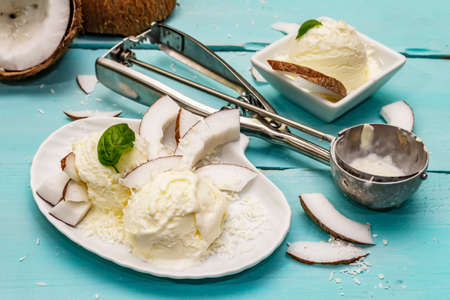 Lactose free coconut ice cream. Special spoon, halves of fruit, flakes. Vegan dessert concept. Trendy turquoise wooden boards backgroundの写真素材