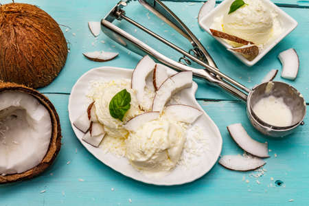 Lactose free coconut ice cream. Special spoon, halves of fruit, flakes. Vegan dessert concept. Trendy turquoise wooden boards backgroundの写真素材