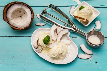 Lactose free coconut ice cream. Special spoon, halves of fruit, flakes. Vegan dessert concept. Trendy turquoise wooden boards backgroundの写真素材