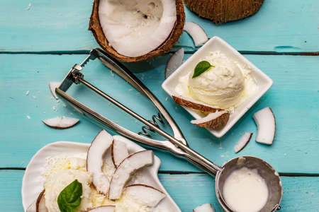 Lactose free coconut ice cream. Special spoon, halves of fruit, flakes. Vegan dessert concept. Trendy turquoise wooden boards backgroundの写真素材