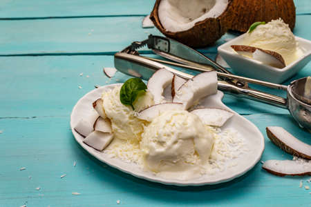 Lactose free coconut ice cream. Special spoon, halves of fruit, flakes. Vegan dessert concept. Trendy turquoise wooden boards backgroundの写真素材