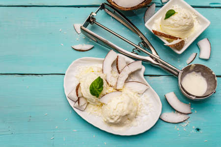 Lactose free coconut ice cream. Special spoon, halves of fruit, flakes. Vegan dessert concept. Trendy turquoise wooden boards backgroundの写真素材