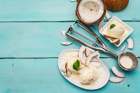 Lactose free coconut ice cream. Special spoon, halves of fruit, flakes. Vegan dessert concept. Trendy turquoise wooden boards background, top viewの写真素材