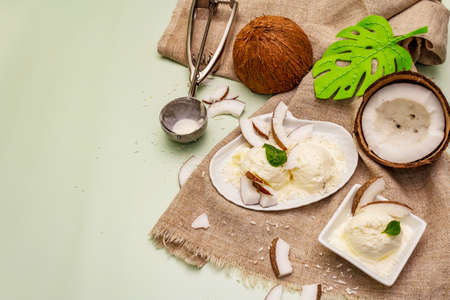 Lactose free coconut ice cream. Special spoon, halves of fruit, flakes. Vegan dessert concept. Light green background, top viewの写真素材