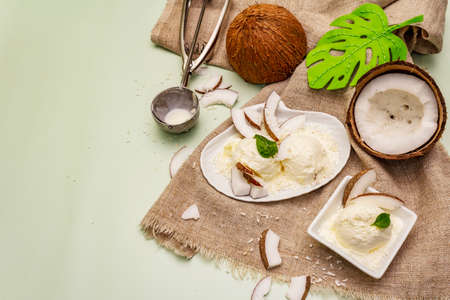 Lactose free coconut ice cream. Special spoon, halves of fruit, flakes. Vegan dessert concept. Light green background, top viewの写真素材