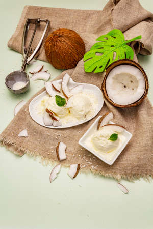 Lactose free coconut ice cream. Special spoon, halves of fruit, flakes. Vegan dessert concept. Light green backgroundの写真素材