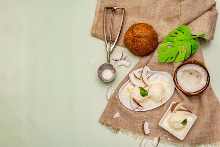 Lactose free coconut ice cream. Special spoon, halves of fruit, flakes. Vegan dessert concept. Light green background, top viewの写真素材