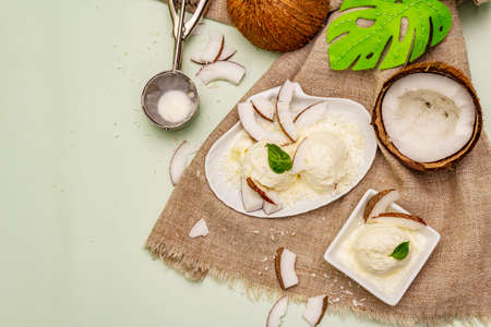 Lactose free coconut ice cream. Special spoon, halves of fruit, flakes. Vegan dessert concept. Light green background, top viewの写真素材