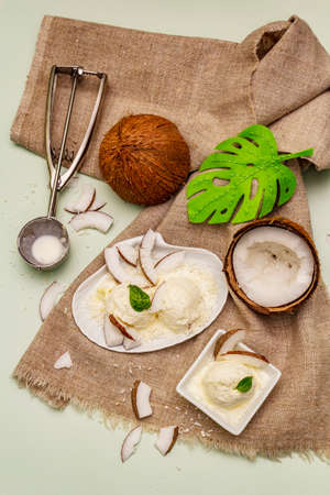Lactose free coconut ice cream. Special spoon, halves of fruit, flakes. Vegan dessert concept. Light green backgroundの写真素材