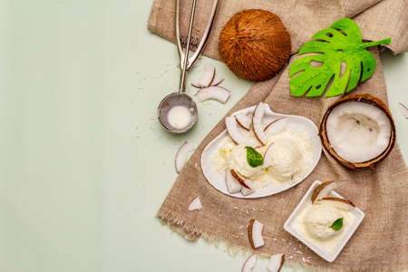 Lactose free coconut ice cream. Special spoon, halves of fruit, flakes. Vegan dessert concept. Light green background, top viewの写真素材