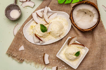 Lactose free coconut ice cream. Special spoon, halves of fruit, flakes. Vegan dessert concept. Light green backgroundの写真素材