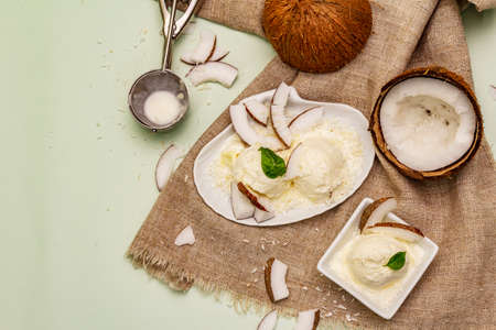 Lactose free coconut ice cream. Special spoon, halves of fruit, flakes. Vegan dessert concept. Light green backgroundの写真素材