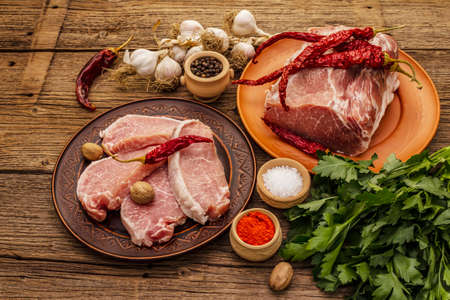 Assorted raw pork meat. Fresh loin, spices, fragrant vegetables and parsley. Vintage wooden boards table, close upの写真素材