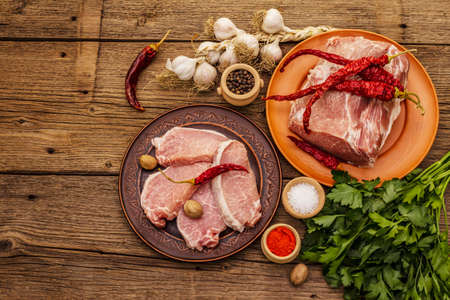 Assorted raw pork meat. Fresh loin, spices, fragrant vegetables and parsley. Vintage wooden boards table, top viewの写真素材