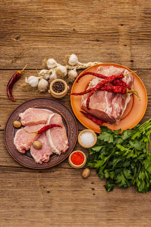 Assorted raw pork meat. Fresh loin, spices, fragrant vegetables and parsley. Vintage wooden boards table, top viewの写真素材