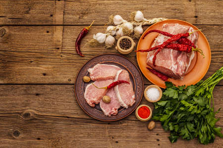 Assorted raw pork meat. Fresh loin, spices, fragrant vegetables and parsley. Vintage wooden boards table, top viewの写真素材