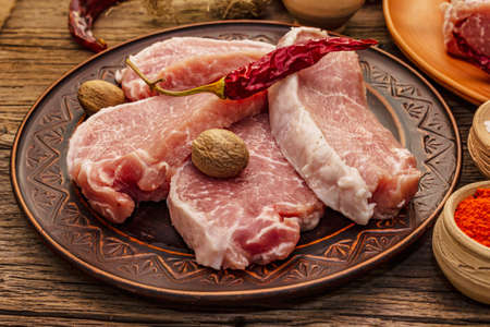 Assorted raw pork meat. Fresh loin, spices, fragrant vegetables and parsley. Vintage wooden boards table, close upの写真素材