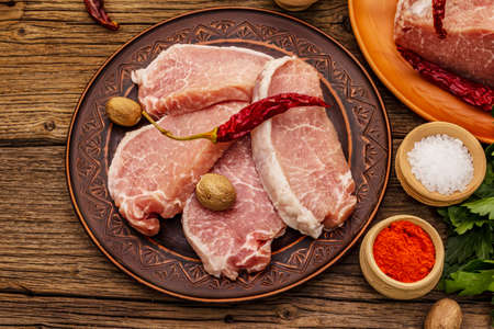 Assorted raw pork meat. Fresh loin, spices, fragrant vegetables and parsley. Vintage wooden boards table, top viewの写真素材