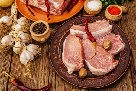 Assorted raw pork meat. Fresh loin, spices, fragrant vegetables and parsley. Vintage wooden boards table, close upの写真素材