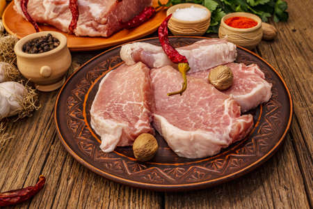 Assorted raw pork meat. Fresh loin, spices, fragrant vegetables and parsley. Vintage wooden boards table, close upの写真素材