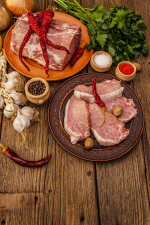 Assorted raw pork meat. Fresh loin, spices, fragrant vegetables and parsley. Vintage wooden boards table, copy spaceの写真素材