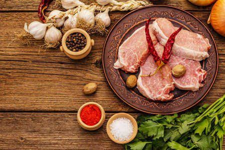 Raw pork meat. Fresh loin, spices, fragrant vegetables and parsley. Vintage wooden boards table, top viewの写真素材