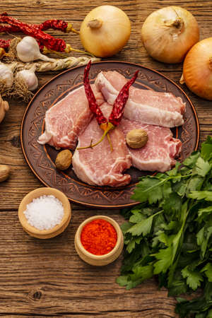Raw pork meat. Fresh loin, spices, fragrant vegetables and parsley. Vintage wooden boards table, copy spaceの写真素材