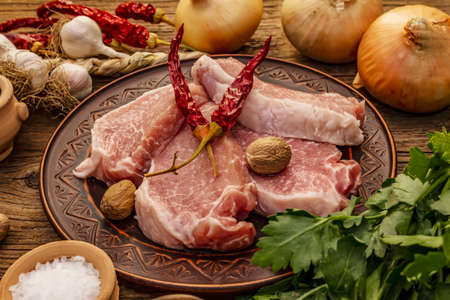Raw pork meat. Fresh loin, spices, fragrant vegetables and parsley. Vintage wooden boards table, close upの写真素材