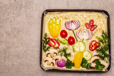 Raw Garden Focaccia. Fresh dough and vegetables, olive oil, greens. Colorful gardenscape, stone concrete backgroundの写真素材