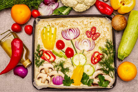 Raw Garden Focaccia. Fresh dough and vegetables, olive oil, greens. Colorful gardenscape, stone concrete backgroundの写真素材