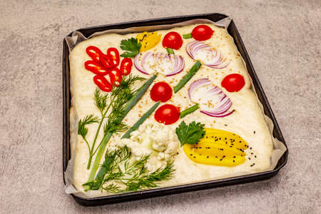Raw Garden Focaccia. Fresh dough and vegetables, olive oil, greens. Colorful gardenscape, stone concrete backgroundの写真素材