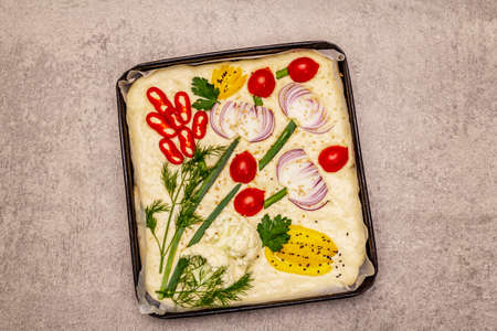 Raw Garden Focaccia. Fresh dough and vegetables, olive oil, greens. Colorful gardenscape, stone concrete backgroundの写真素材