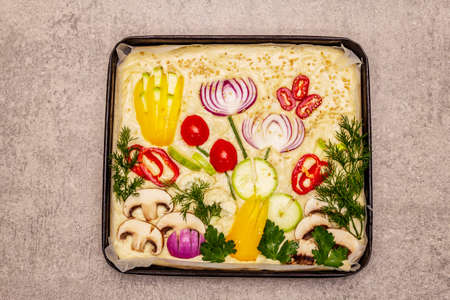 Raw Garden Focaccia. Fresh dough and vegetables, olive oil, greens. Colorful gardenscape, stone concrete backgroundの写真素材