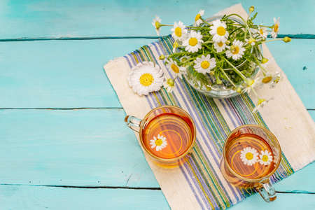 Chamomile tea. Fresh flowers, summer hot drink concept. Alternative medicine, lifestyle. Trendy turquoise wooden boards background, top viewの写真素材
