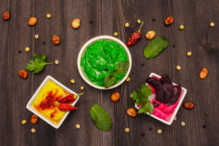 Hummus, healthy vegan (vegetarian) food. Assorted three types: classic, mint and beetroot. Edamame dry beans, spices, fresh leaves. Trendy black wooden boards backgroundの写真素材