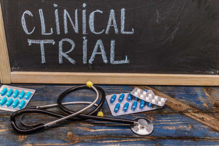 Clinical trial concept. Chalk board, stethoscope, pills. Wooden boards backgroundの写真素材