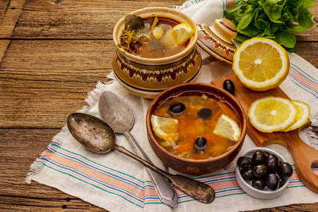 Hodgepodge, hot soup served in traditional ceramic bowl and pot. Classical Eastern Europe dish, old vintage wooden boards backgroundの写真素材
