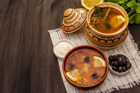 Hodgepodge, hot soup served in traditional ceramic bowl and pot. Classical Eastern Europe dish, trendy black wooden backgroundの写真素材